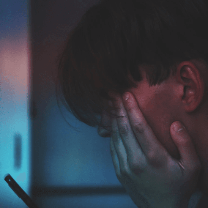 Photo de Adrian Swancar sur Unsplash : un jeune homme regarde l'écran de son téléphone, en se cachant les yeux. 